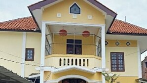 Un bâtiment à deux étages, doté d’une façade jaune, d’un toit recouvert de tuiles rouges et d’un balcon orné de lanternes rouges.