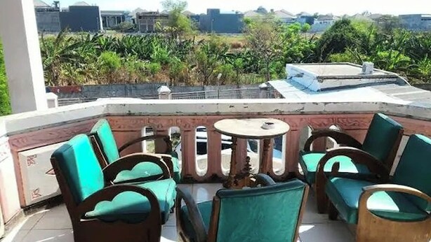 Une terrasse avec des fauteuils à coussins verts et une petite table ronde, donnant sur un jardin et des bâtiments.