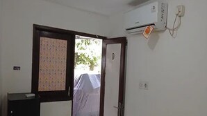 Une pièce avec une porte donnant sur l’extérieur, un climatiseur fixé au mur et un petit bureau avec un ordinateur.