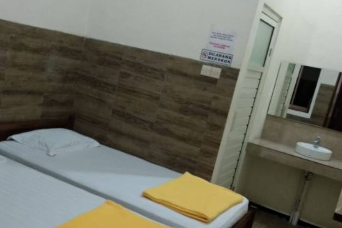 Une chambre simple avec deux lits, une tête de lit en bois, une petite salle de bain avec un lavabo et un miroir, et un panneau sur le mur.