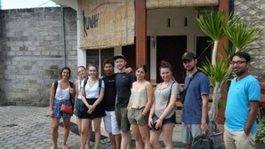Un groupe de personnes se tient devant un bâtiment sur lequel on peut lire l’inscription « RUMAH ».