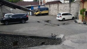 Un espace de stationnement avec un mur en pierre, un camion jaune et deux voitures.