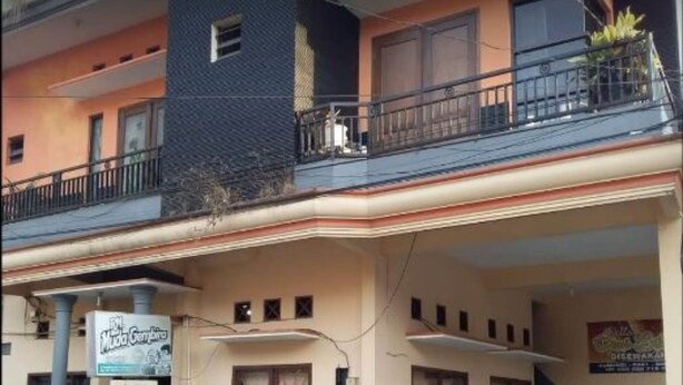 Un edificio a due piani con un balcone al piano superiore. Un cartello è presente al piano terra e un'auto parcheggiata davanti.