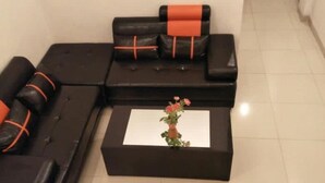 A sectional sofa with orange accents, a small table with a vase of flowers, and a tiled floor. - 7 Dream Hotel (Palembang)