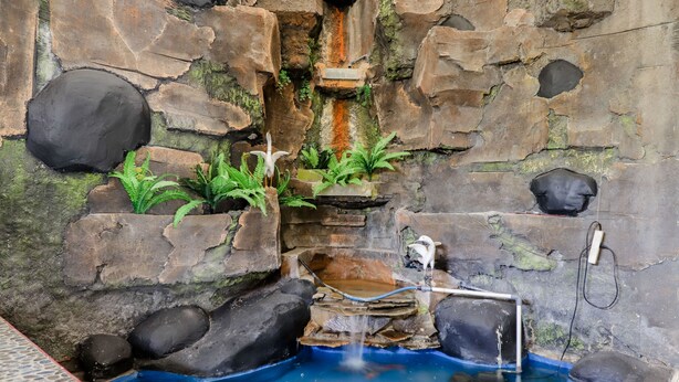 Ein Badebereich aus Stein mit Wasserfall, Pflanzen und einer Holzbank.