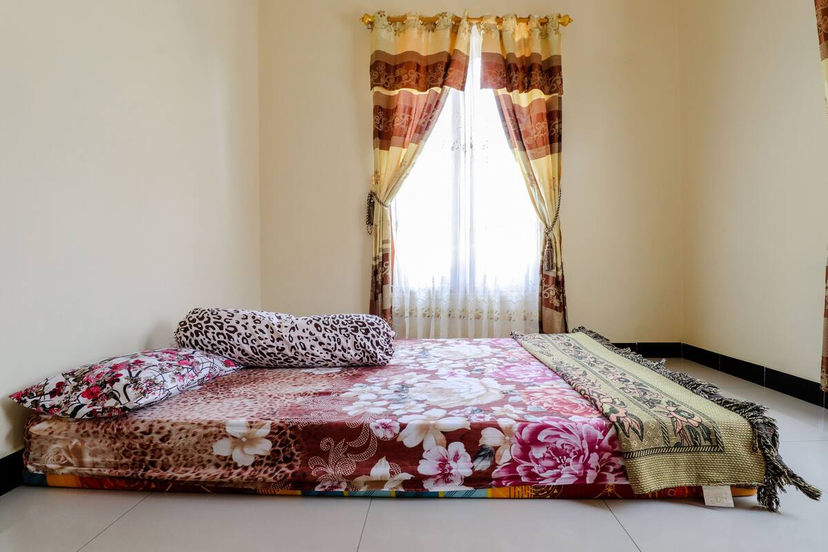 A bedroom with a bed, floral bedspread, leopard print pillow, and a decorative throw.