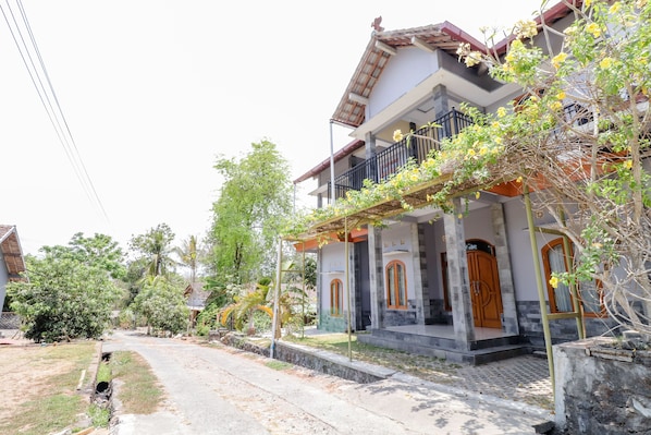 A two-story house with a balcony, a driveway, and surrounding greenery. - Dewisri Homestay (Bantul)