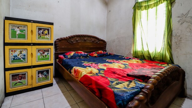 Une chambre à coucher avec un lit en bois, une couvre-lit à motifs floraux et un meuble mural où sont exposés des objets de collection sur le thème du sport.