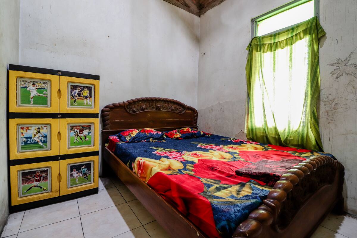 A bedroom with a wooden bed, a floral bedspread, and a wall-mounted cabinet with sports memorabilia.
