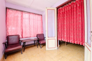 Una habitación con dos sillas, una mesita y una ventana con cortinas rojas.