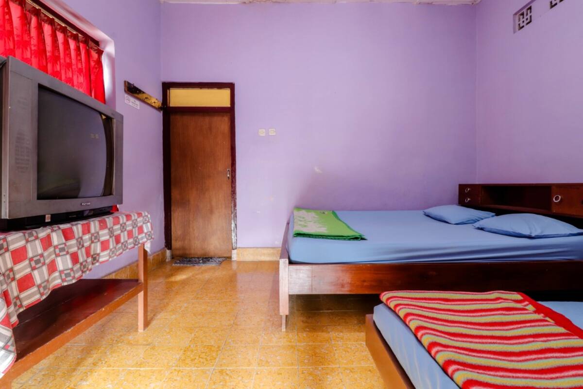 A room with a bed, a television on a stand, a wooden door, and a tiled floor.