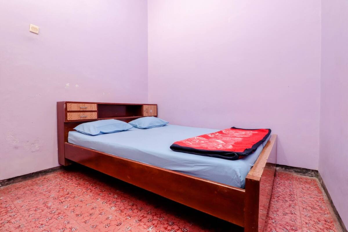 A single bed with a wooden frame, a blue mattress, and a red blanket.