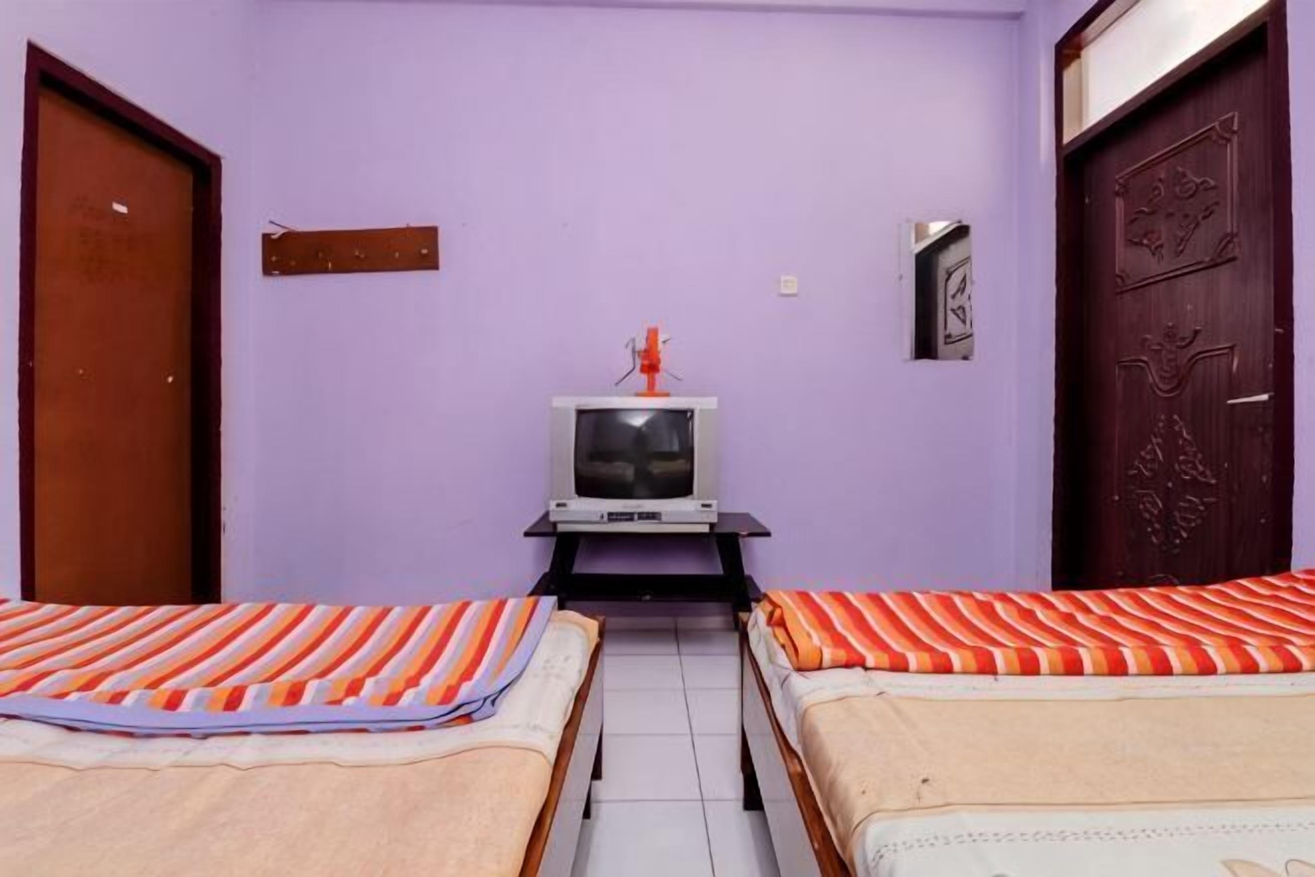 Quarto com duas camas, televisão e uma porta.