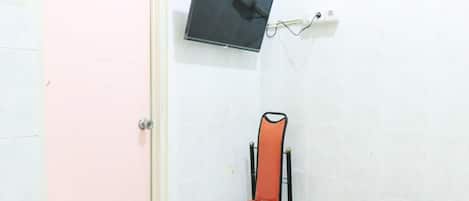 A small room with a pink door, a black TV mounted on the wall, and a red and black chair with a blue cushion.