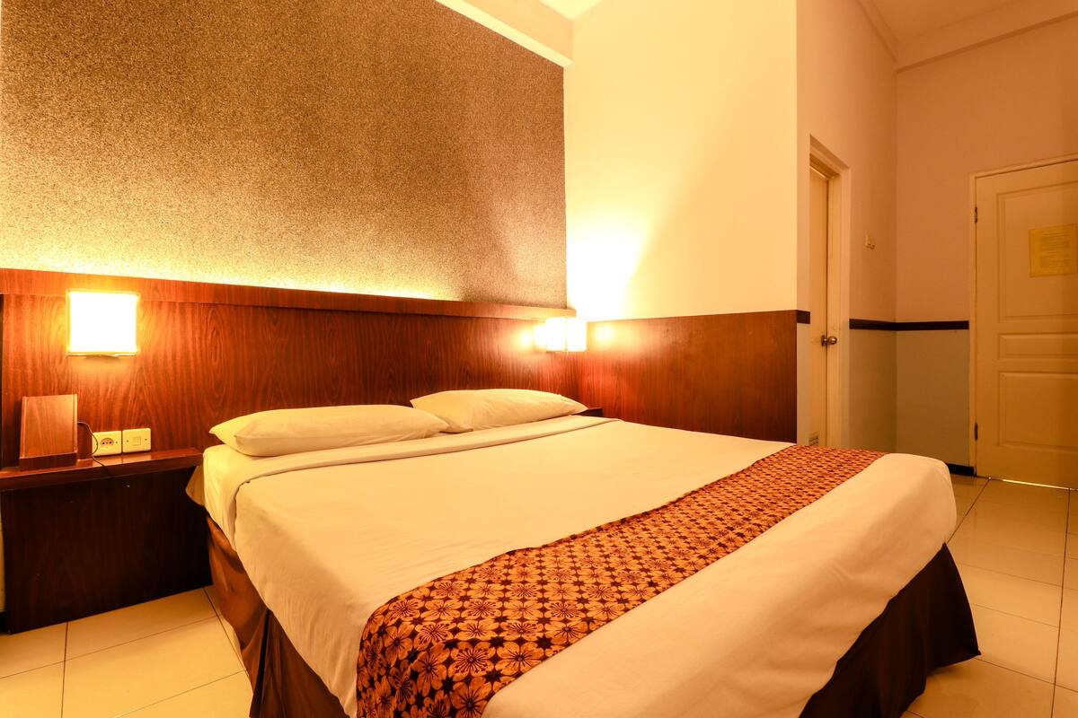 Una habitación de hotel con una cama grande, cabecera de madera, lámparas de noche y una puerta con un letrero.