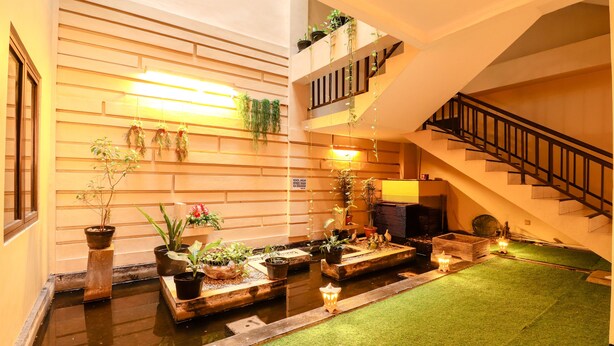 Um espaço amplo e interno com um espelho d'água central, diversas plantas em vasos e uma escada que leva a um andar superior.