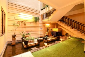 A spacious indoor area with a central water feature, multiple potted plants, and a staircase leading to an upper level. - Hotel Jawa by Zuzu (Surabaya)