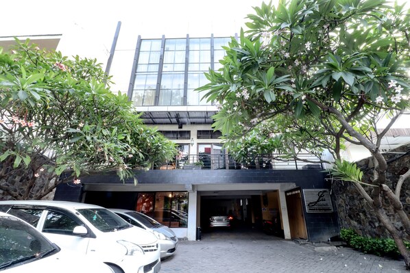 A modern building with a glass facade, a covered entrance, and a parking area with several cars. - Hotel Jawa by Zuzu (Surabaya)