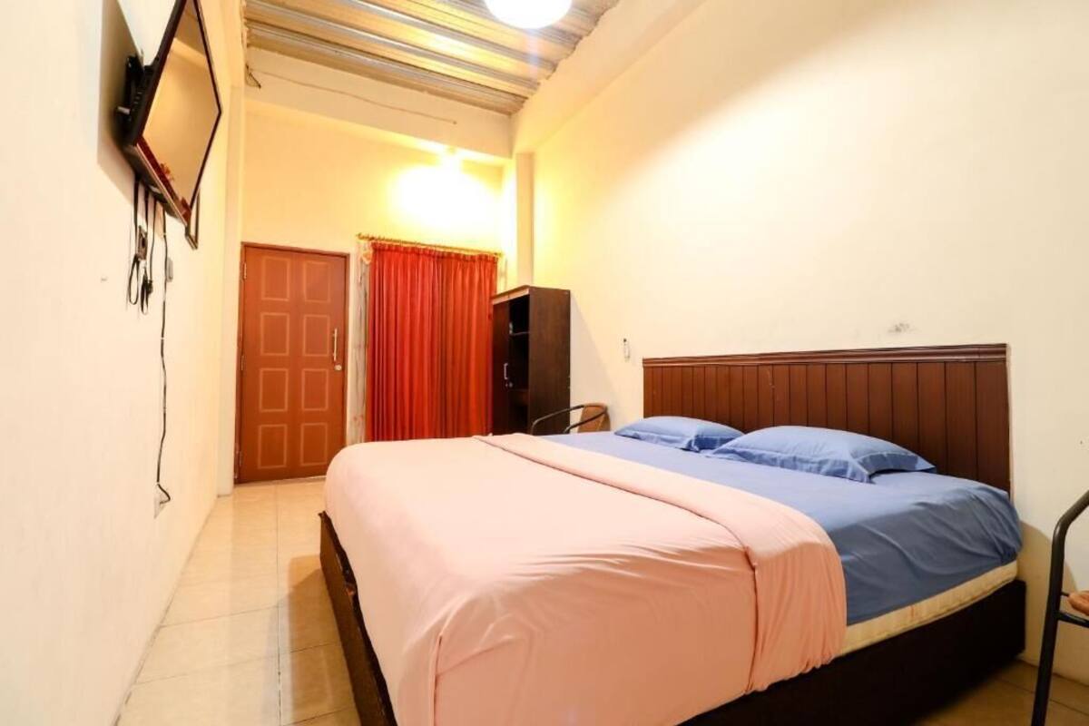 A bedroom with a bed, a television mounted on the wall, a door, and a red curtain.