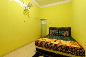 A small, brightly colored room with a bed, a fan, and a door. - Willy Homestay (Borobudur)