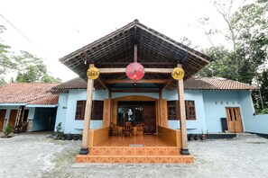 A traditional building with a tiled roof, a wooden porch, and a red umbrella. - Willy Homestay (Borobudur)
