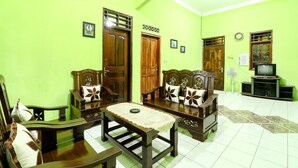 A living room with green walls, wooden furniture, a television, and a fan. - Willy Homestay (Borobudur)