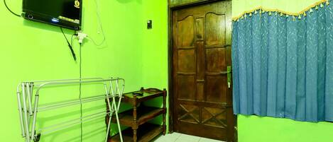 A room with a green wall, a wooden door with a blue curtain, a TV mounted on the wall, and a metal drying rack.