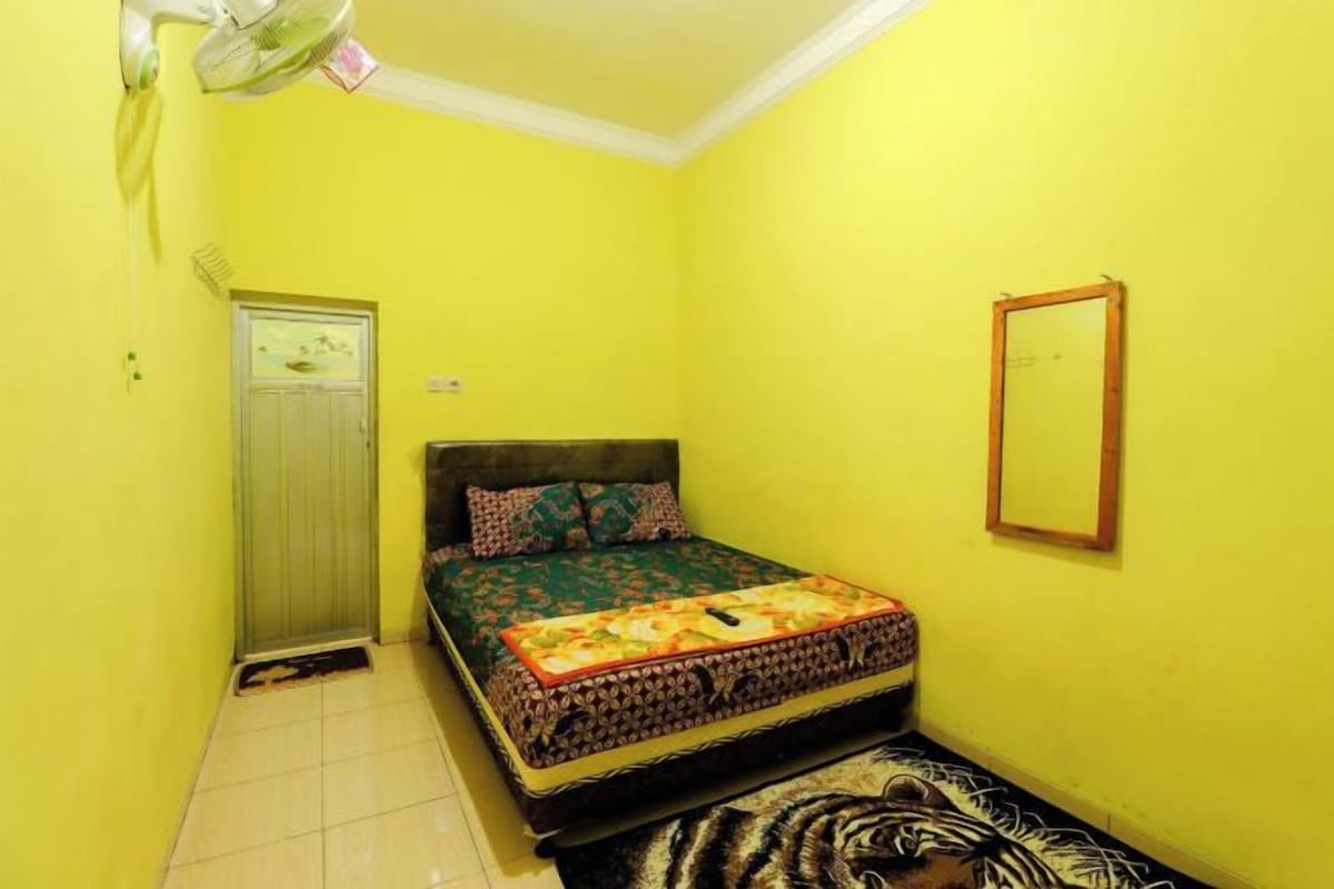 Una habitación con cama, puerta, espejo y ventilador.