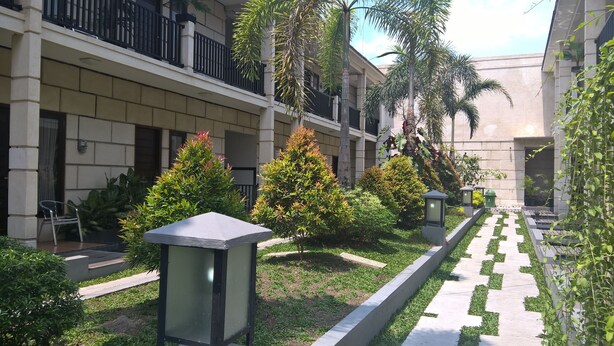 A courtyard with a pathway, potted plants, and a building with balconies. - Rumah Amanda Residence (Palangkaraya)