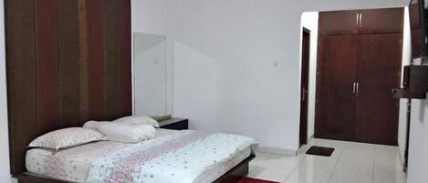 A bedroom with a bed, a red rug, a wardrobe, and an air conditioning unit.