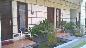 A covered outdoor area with a wooden deck, potted plants, and a chair. - Rumah Amanda Residence (Palangkaraya)