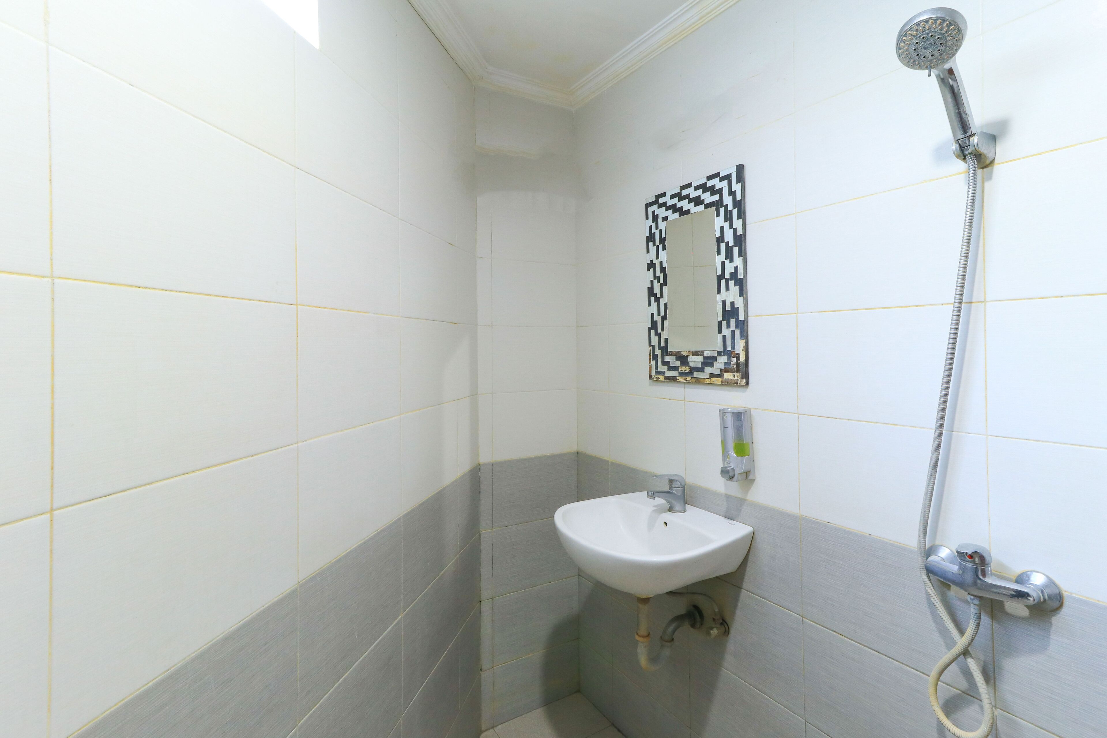 A bathroom with white and gray tiles, a white sink, a handheld showerhead, and a wall-mounted mirror.