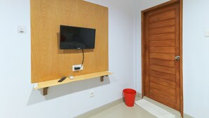A room with a mounted TV on a wooden panel, a door, and a red bucket on the floor. - deSeruni Guest House (Dalung)