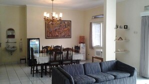 A living room with a sofa, a dining table with chairs, a chandelier, a painting, and a TV. - Rumah Anda Guest House (Bandung)