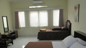 A hotel room with a large bed, a desk, a chair, a dresser, and a window with curtains. - Rumah Anda Guest House (Bandung)