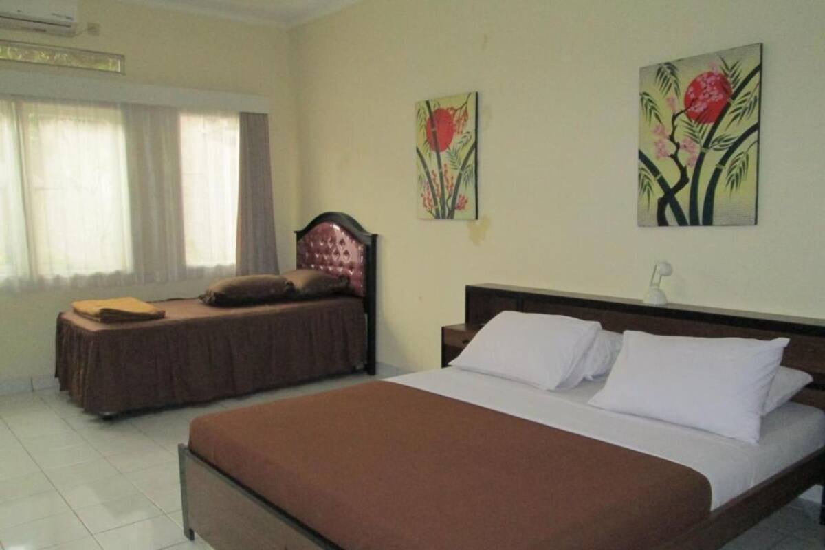 A hotel room with a large bed, a smaller bed, and a window with curtains.