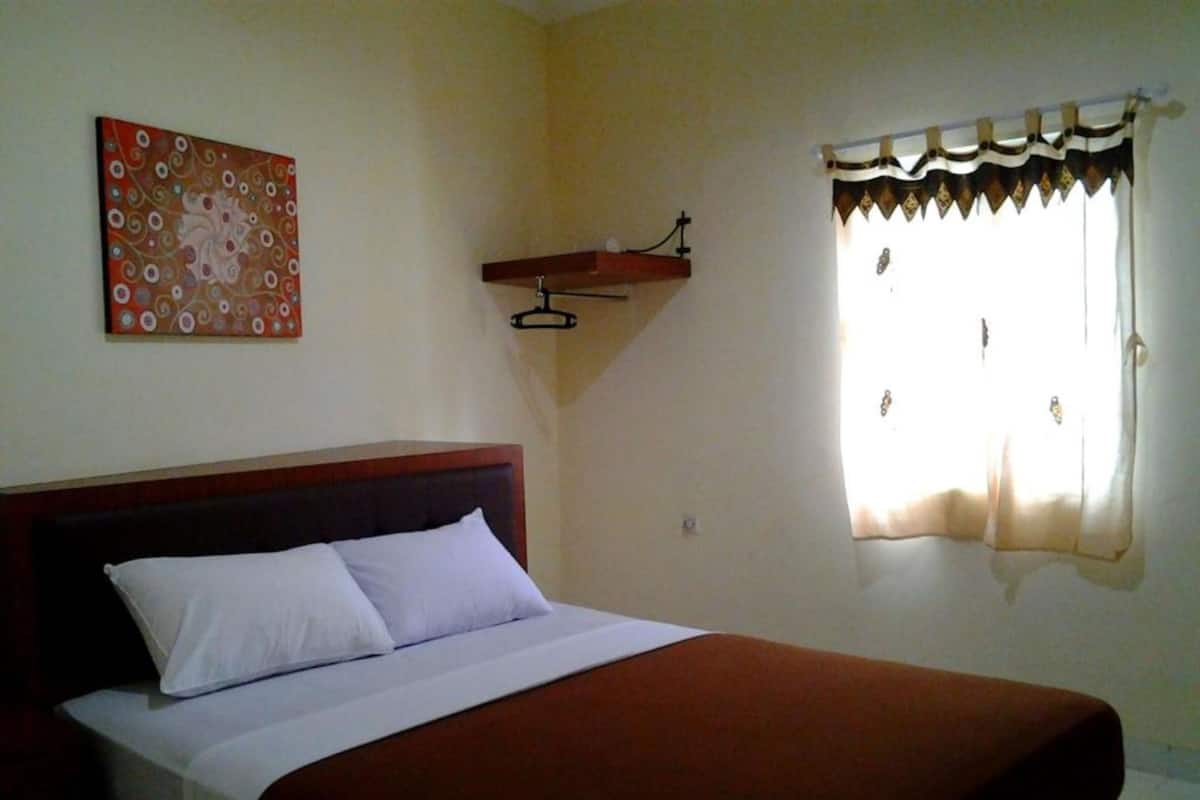 A bed with a wooden headboard, a white pillow, and a brown bedspread. There is a wall hanging with a floral pattern above the bed.
