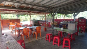 Un café al aire libre con mesas y sillas, un refrigerador de Coca-Cola y un letrero que indica Warung Tower.