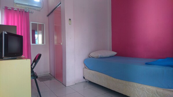 Ein Zimmer mit einem Bett, einem Fernseher auf einem Schreibtisch, einem Fenster mit rosa Vorhängen und einer Tür.