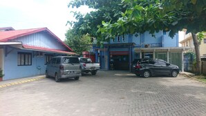 Un edificio de techo rojo y fachada azul, con mostrador de recepción y vehículos estacionados.