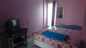 Una habitación con cama, escritorio con televisor, espejo y ventana con cortinas.