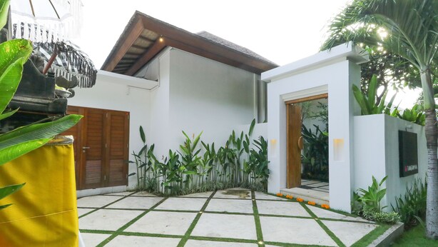 Una casa moderna con un patio empedrado, una puerta de madera y una pared blanca.