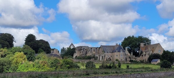 A historic stone building with multiple towers and a large central tower, surrounded by lush greenery and a partly cloudy sky.