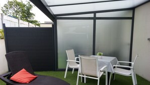 Une terrasse avec un fauteuil de relaxation noir, une table blanche et quatre chaises blanches.