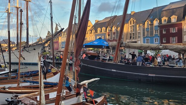 Un port où des bateaux sont amarrés, une foule de personnes et, au loin, des bâtiments aux couleurs vives.