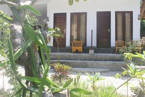 A building with three wooden doors, a set of steps leading to a porch, and two wooden chairs. - Villa Green House (Penida Island)