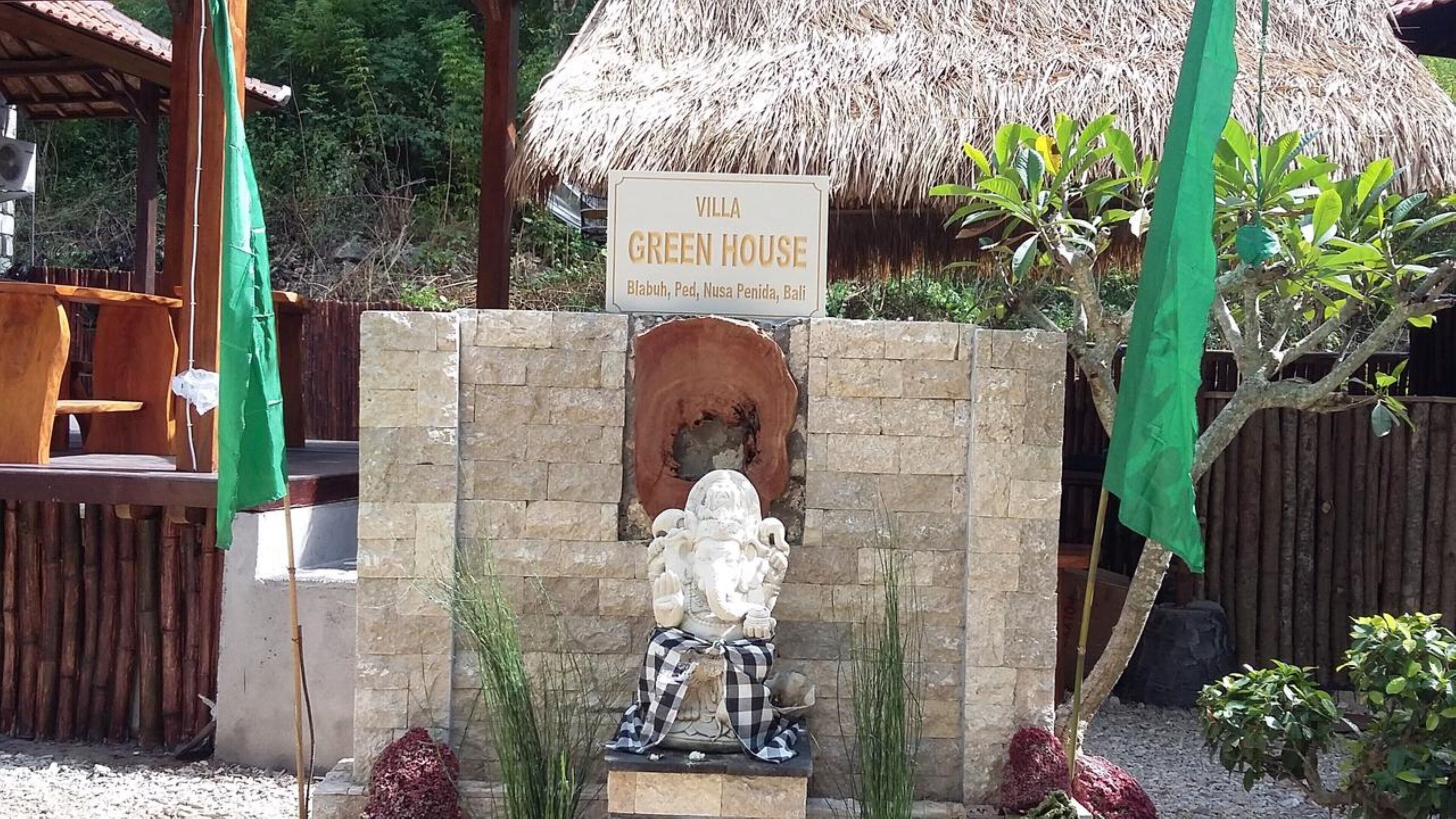 A villa named 'Green House' with a stone statue of a seated figure, a thatched roof structure, and a signboard.