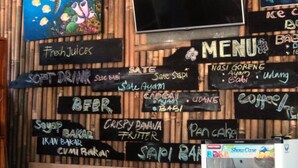 Una pared con diversas opciones de comida y bebida listadas, como jugos frescos, refrescos, cerveza y café.