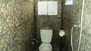 Un baño con pared de piedra, inodoro, ducha y calentador de agua.