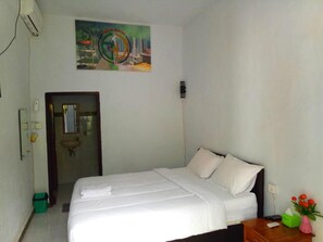 A hotel room with a bed, a small table with a vase of flowers, and a painting on the wall.